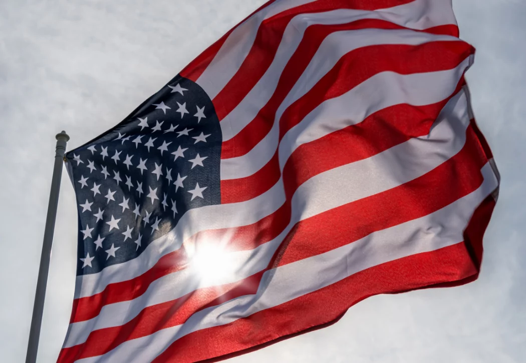 Image of American Flag with sun shining behind it.